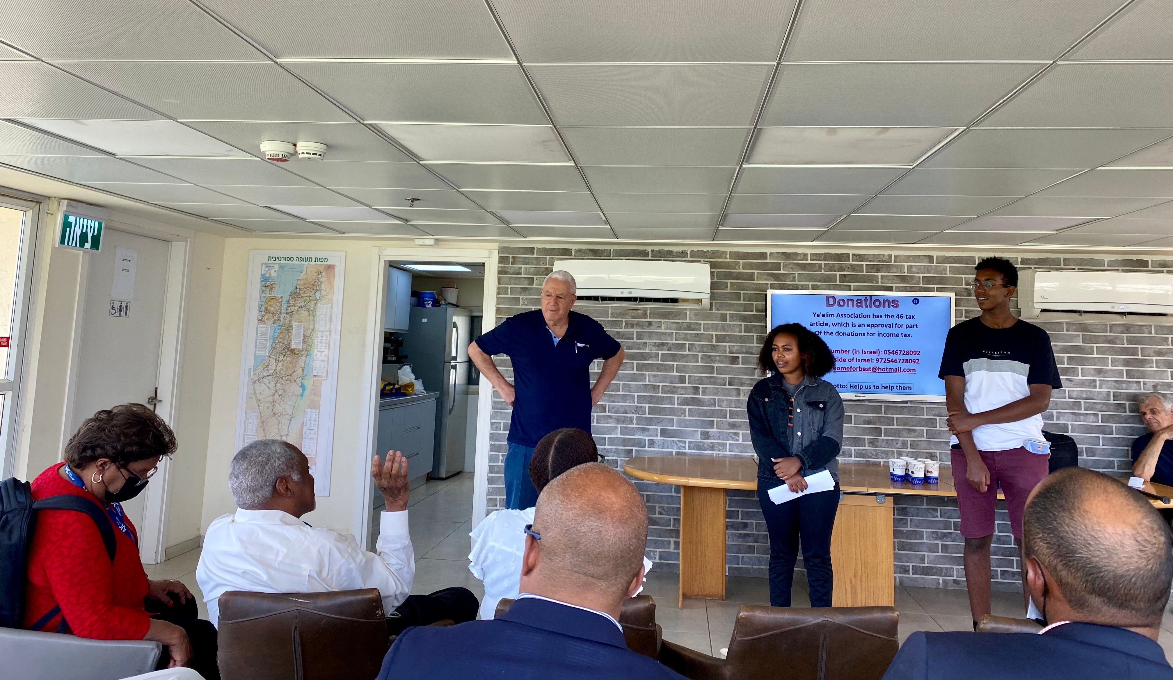 Two Black students and a white man speak to the assembled HBCU presidents. The exit sign over the door is written in Hebrew.